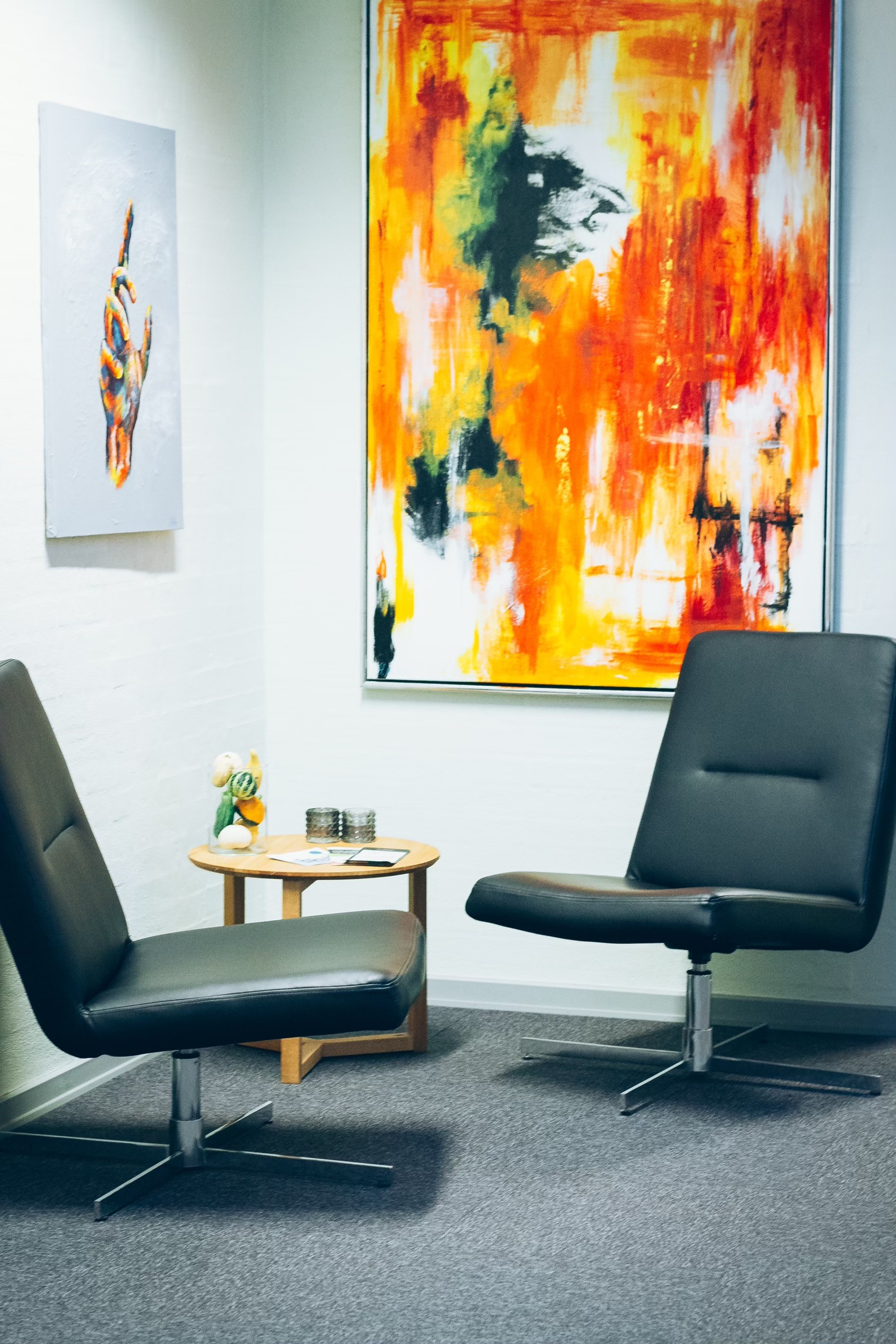 To tomme stole i et hjørne af et kontor med farverige malerier bagved